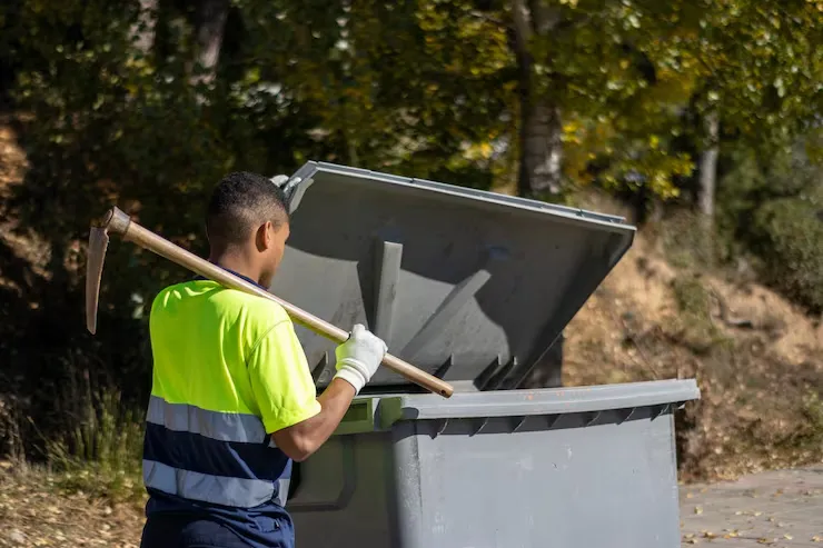back-view-latino-municipal-garbage-worker-uniform-throwing-garbage-into-dumpster-with-sickle-his-shoulder_394312-1349_converted